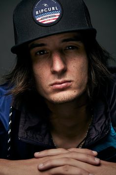 a man with long hair wearing a black hat and jacket is looking at the camera