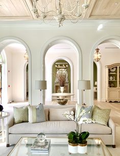 a living room filled with furniture and a chandelier above a glass top coffee table