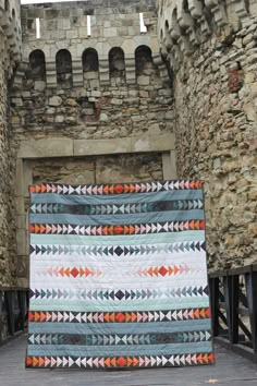 a quilt is displayed in front of an old stone castle wall with arches and doorways