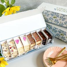 an assortment of desserts in a box next to a plate with flowers on it