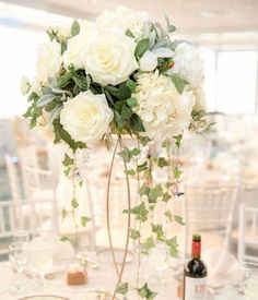 a tall vase filled with white flowers sitting on top of a table next to wine glasses