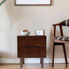 a small wooden table with a clock on it next to a chair and a plant