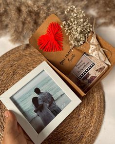 a person holding an open box with a photo on it and a red heart hanging from the top