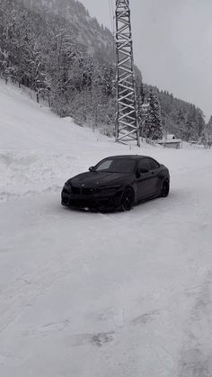 a black car driving down a snow covered road next to a tall metal structure in the background