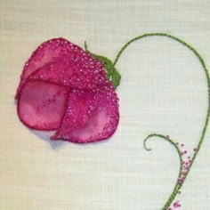 a pink flower with green stems on a white tableclothed surface, next to a needle and thread