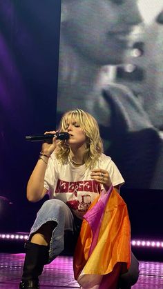 a woman sitting on top of a stage holding a microphone in her right hand and wearing knee high boots