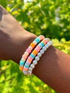 two bracelets with multicolored beads and pearls are on the arm of a person