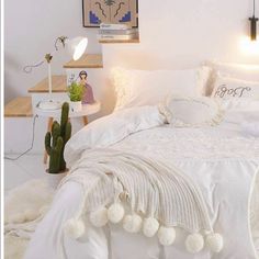 a white bed with pom - poms on it and a cactus in the corner