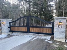 a driveway gate with two stone pillars and a light on the top, in front of some trees