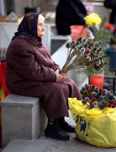 an old woman sitting on a bench with flowers