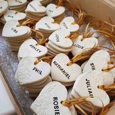 some white heart shaped cookies with names on them in a cardboard box, tied with twine