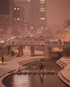 people are walking on the sidewalk next to a river and bridge at night in winter