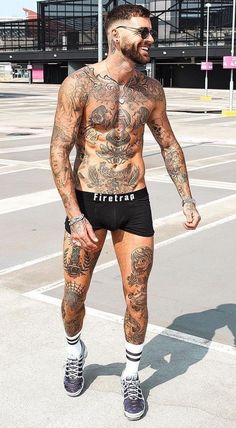 a man with tattoos on his body standing in the middle of an empty parking lot