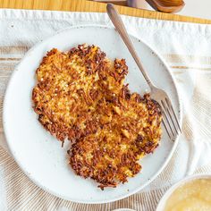 two hash browns on a white plate with a fork next to some dipping sauces