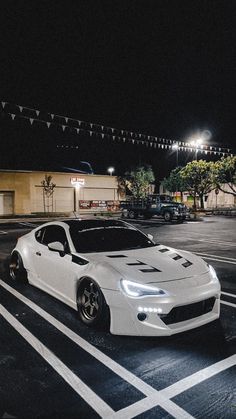 a white sports car is parked in the parking lot at night with its lights on