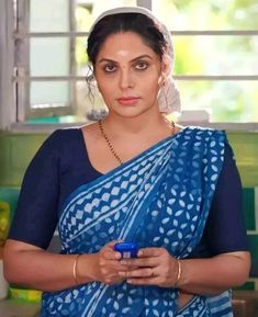 a woman wearing a blue sari holding a cup in her hands and looking at the camera