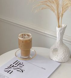 there is a drink on the table next to a vase with some grass in it