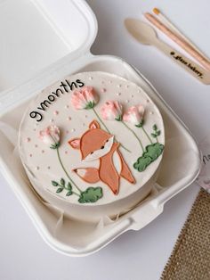 a decorated cake in a plastic container with flowers and an animal on the side that says someone