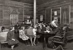 an old black and white photo of children sitting at desks in a room with american flags on the walls