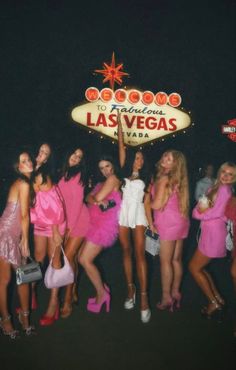 a group of women posing in front of the las vegas sign with pink dresses and high heels