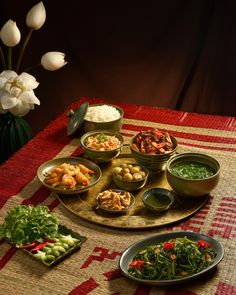 a table topped with bowls filled with different types of food next to white tulips