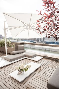 an outdoor living area with couches, tables and umbrellas over looking the water