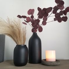 two black vases with dried flowers and a lit candle