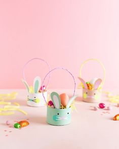 three small easter baskets with bunny ears and eggs in them on a pink tablecloth