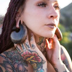 a woman with tattoos and piercings on her chest is talking on the phone while wearing ear rings