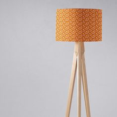 an orange and white floor lamp with a wooden tripod base on a grey background