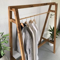 clothes hanging on wooden hangers in front of a white wall and potted plant