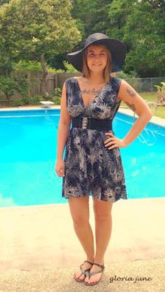 a woman standing in front of a swimming pool wearing a black hat and blue dress