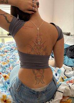 a woman with tattoos on her back sitting on a bed