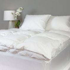 an unmade bed with white sheets and pillows on it, next to a lamp