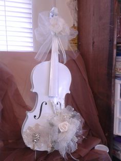 a white violin decorated with flowers and pearls on a brown clothed chair in front of a window