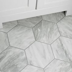 a bathroom floor with hexagonal tiles and white cabinetry in the corner,