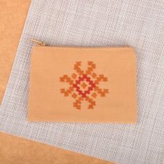 an orange and red cross stitched pouch sitting on top of a piece of fabric