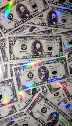 a pile of one hundred dollar bills sitting on top of each other with colored lights coming from them