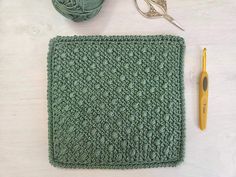 a crochet square with yarn, scissors and knitting needles on a white table