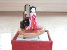 a doll is sitting on top of a red box with a mirror and suitcase in it