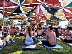 a group of people doing yoga on mats under umbrellas at an outdoor event in the sun