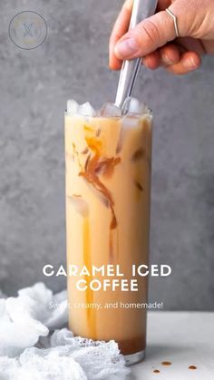 someone is holding a spoon in a tall glass filled with ice and caramel colored liquid