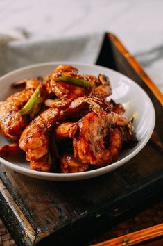 a white bowl filled with fried food on top of a wooden table next to chopsticks