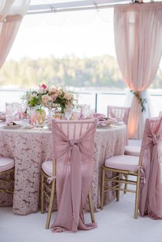 the table is set with pink linens and chairs for an elegant wedding reception at the lake house