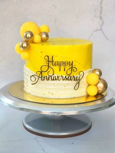 a yellow and white birthday cake on a silver platter with the words happy anniversary written on it