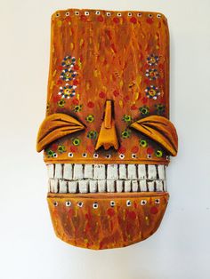 an orange mask with white teeth is hanging on the wall and it's made out of wood