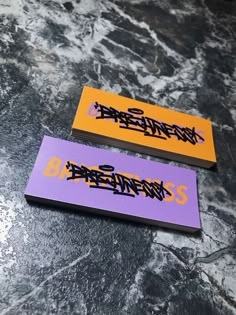 two business cards sitting on top of a marble table with graffiti written on them in purple and orange