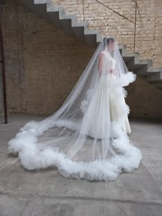 a woman in a white wedding dress with a veil on her head standing next to a stair case