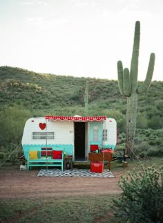 an rv parked next to a cactus in the desert with its door open and two chairs outside