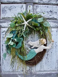 a wreath is hanging on the side of a door with sea shells and greenery